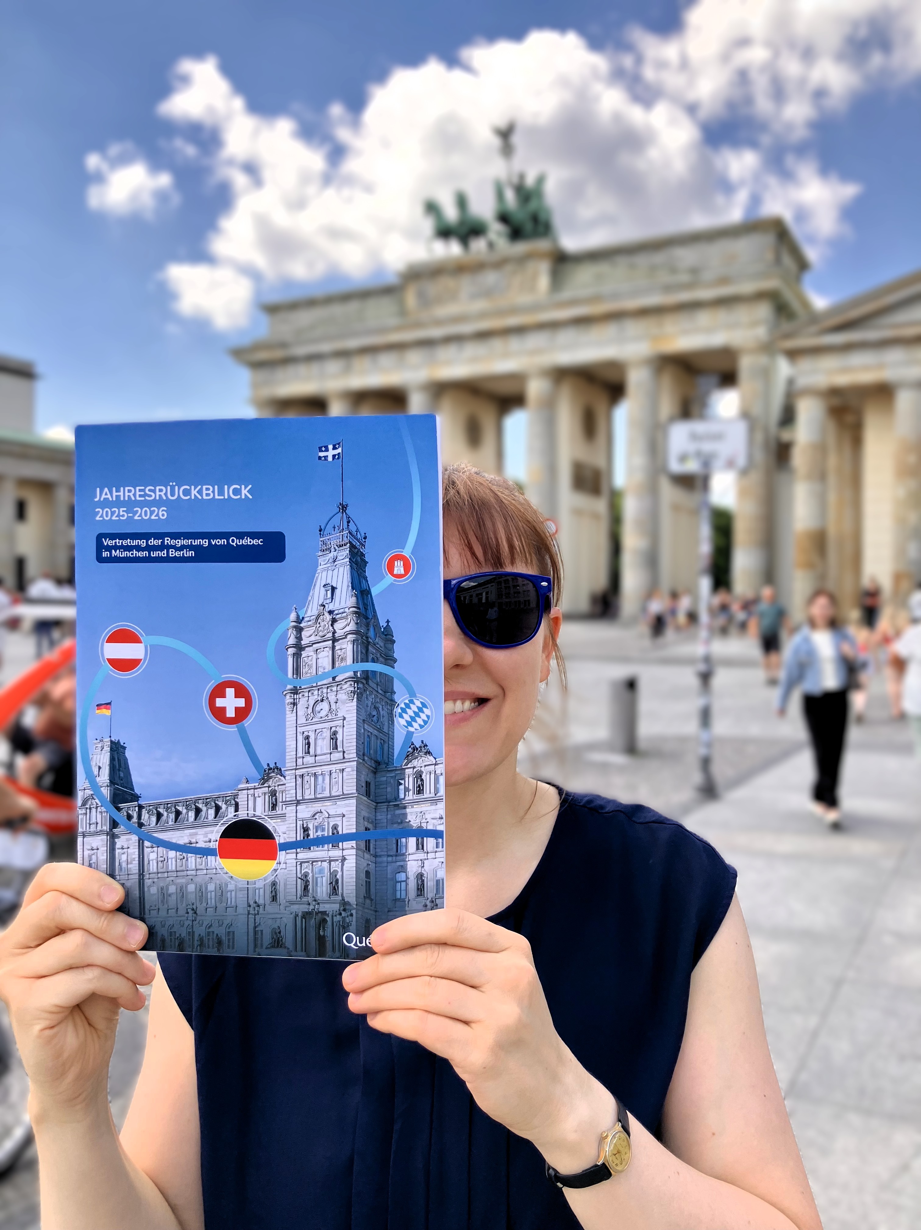Eine Person, die den neuen Jahresrückblick vor ihr Gesicht hält und vor dem Brandenburger Tor steht.