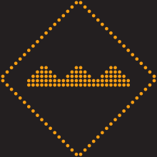 Un pictogramme lumineux en forme de losange. En son centre, trois bosses sont positionnées l’une à la suite de l’autre.