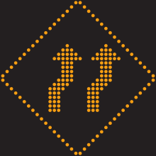 Un pictogramme lumineux en forme de losange. Deux flèches en son centre forment une légère déviation vers la droite.