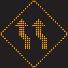 Un pictogramme lumineux en forme de losange. Deux flèches en son centre forment une légère déviation vers la gauche.