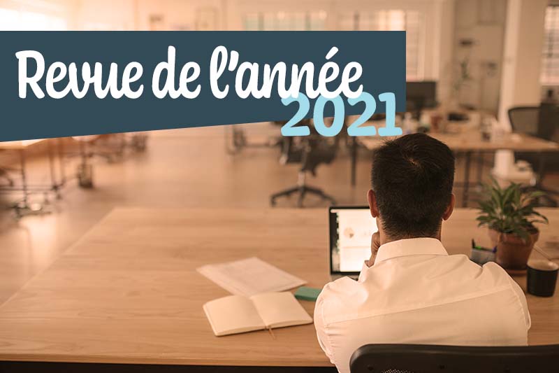 Un homme de dos installé à une table consulte sa tablette. Sur l'image est écrit Revue de l'année 2021.
